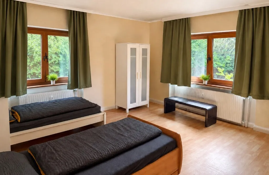 Helles Zweibettzimmer im Gelben Gästehaus mit Schrank, Fenster und Blick ins Grüne