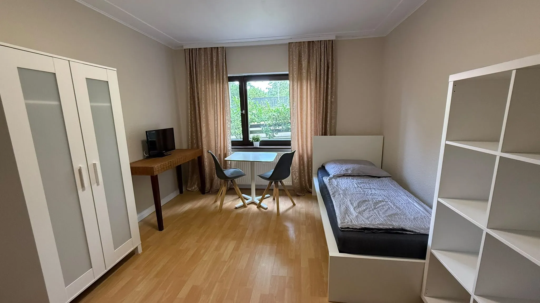 Zimmer mit Bett, Tisch, Fernseher und Fensterfront